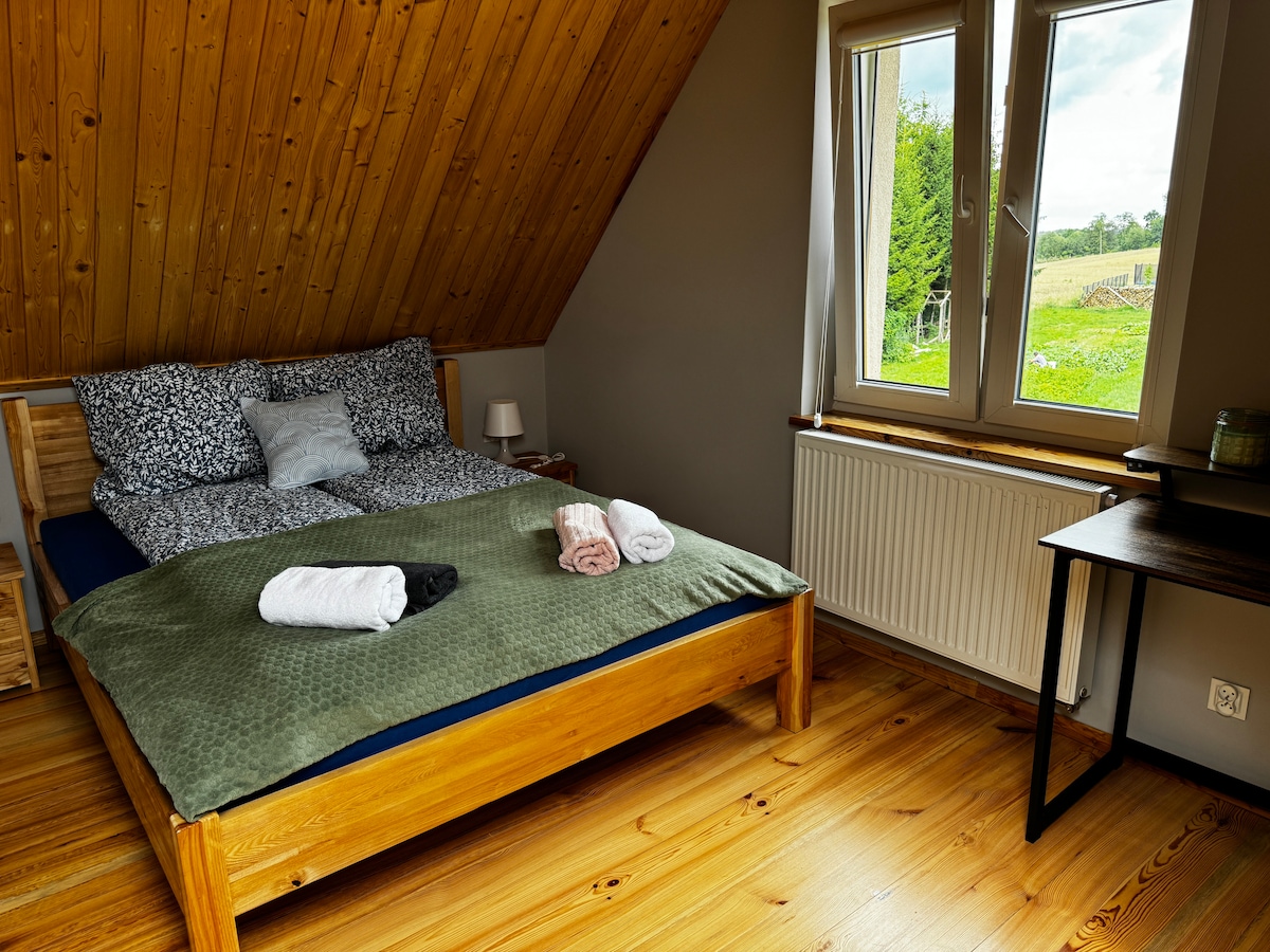 Dormitorio 1 con una cama doble y un escritorio. La ventana da al estanque y al bosque
