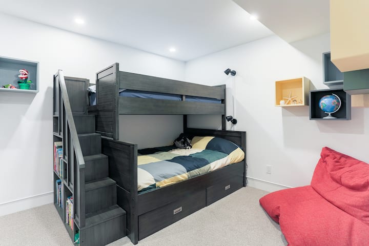 Razigrana soba s modernim krevetima na kat i ugrađenim prostorima za odlaganje. Osmišljen je kako bi zadovoljio djecu jarkim bojama, udobnim tabureom i ugodnom atmosferom za igru i odmor.