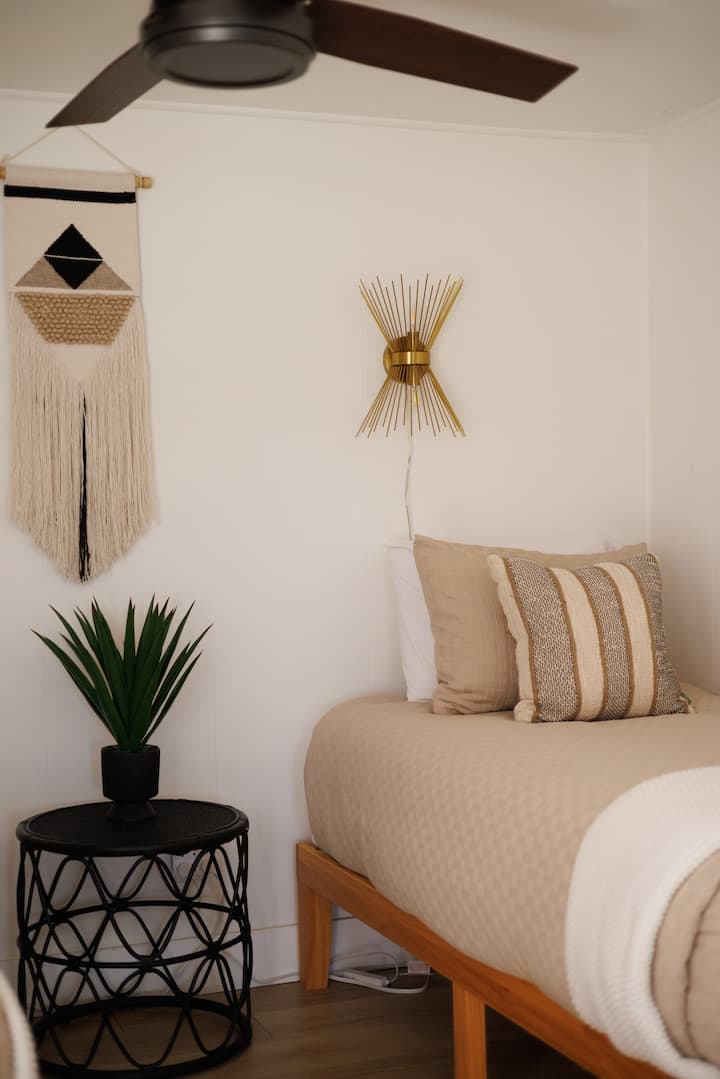 - Близък план на стена с творби в бохо стил и златен осветител   - Топлите тонове и текстури създават спокойна атмосфера   - Спалня в Airbnb с уютен декор, вдъхновен от пустинята  