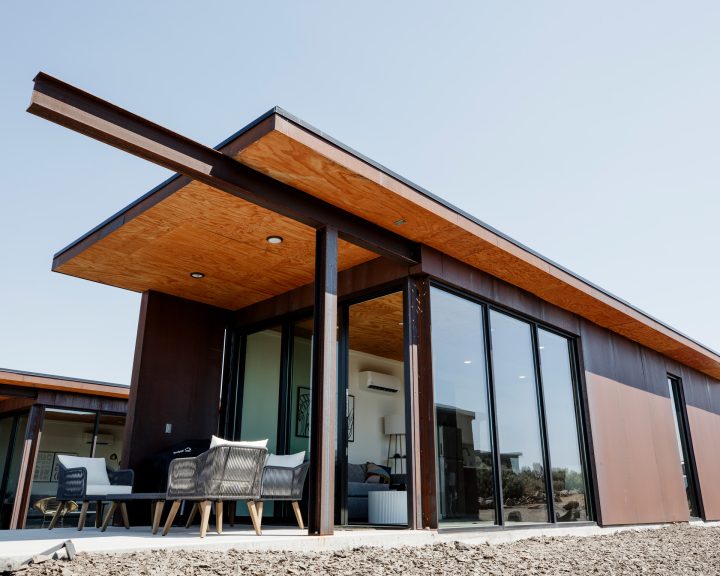 The modern exterior of the condo is characterized by sleek lines and a flat roof. Large glass windows allow natural light to fill the interior, while a covered patio area is furnished with comfortable seating, inviting relaxation in an outdoor setting.
