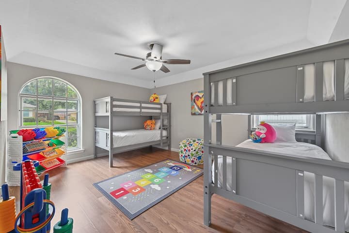 Dhomë argëtuese dhe shumëngjyrëshe për fëmijë me dy krevate dopio gri, shtroja të bardha dhe lodra prej pelushi. Një qilim i ndritshëm hopscotch, raft lodrash dhe qese me fasule polka shtojnë argëtim. Ventilatori i madh i dritareve dhe tavanit e mbajnë hapësirën të ndritshme, të ajrosur dhe të përsosur për të vegjlit.