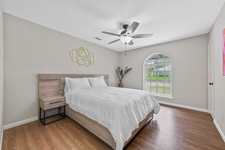 Dhomë gjumi e thjeshtë dhe e ajrosur me një krevat dopio "queen", kornizë druri të lehtë dhe shtroja të bardha të freskëta. Përmban një ventilator modern tavani, art abstrakt muri dhe një dritare të madhe me hark që e mbush hapësirën me dritë natyrale. Dyshemeja e ngrohtë prej druri shton një prekje të rehatshme.