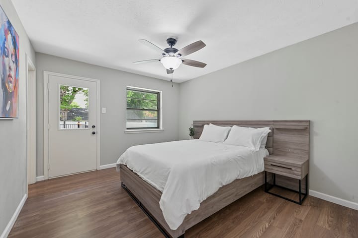 Dhomë gjumi e ndritshme me një krevat dopio "queen", kornizë druri të lehtë dhe shtroja të bardha. Ka një ventilator tavani, banjë private dhe hyrje të drejtpërdrejtë në oborrin e pasmë. Një portret i gjallë abstrakt shton një prekje moderne dhe drita natyrale e mbush dhomën përmes dy dritareve.