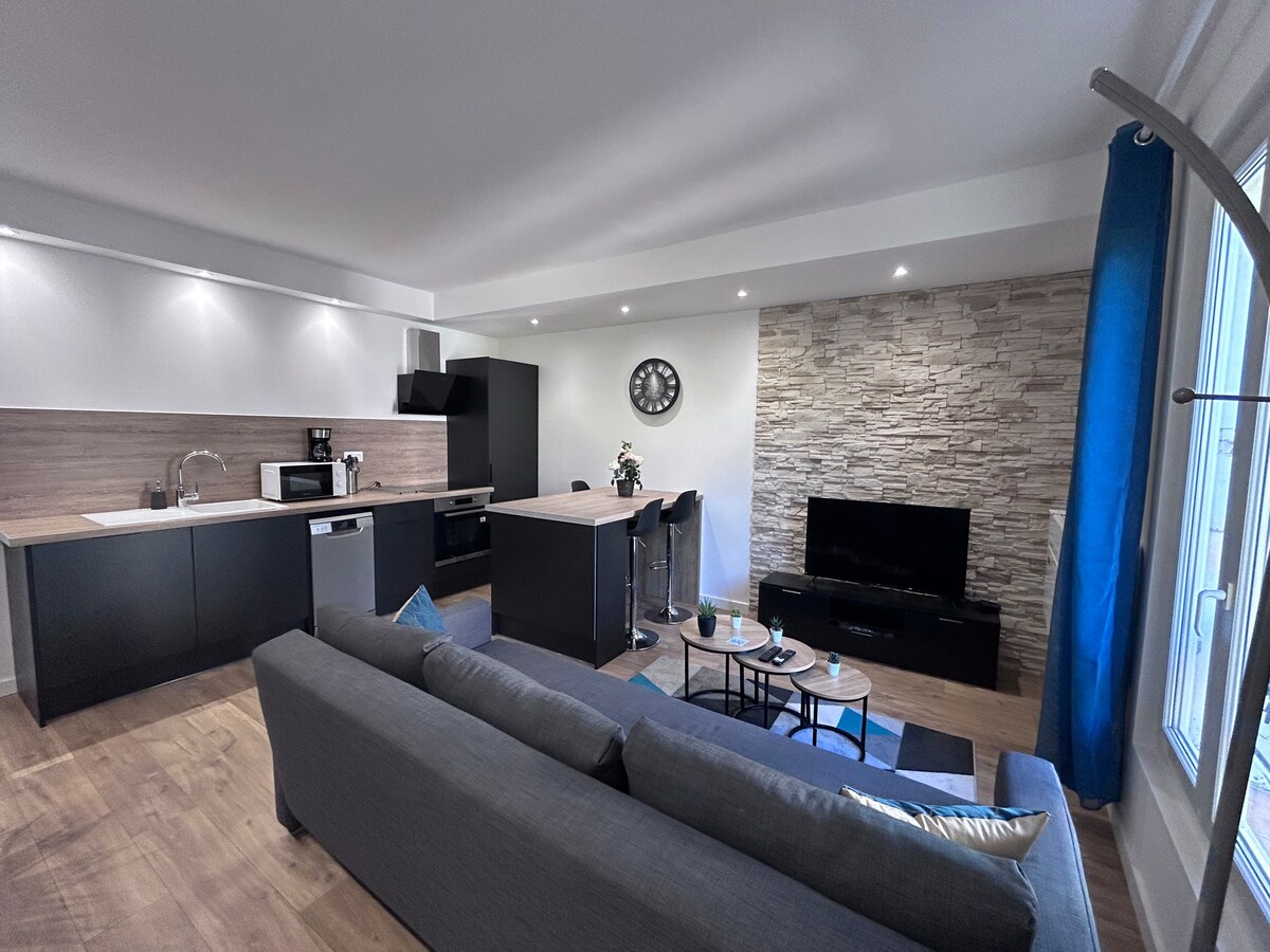 An open living space is featured, showcasing a modern kitchen with black cabinetry and stainless steel appliances, including a microwave. A comfortable gray sofa faces a mounted television, and a round coffee table is positioned on a light area rug. Accents of blue are present, enhancing the ambiance.