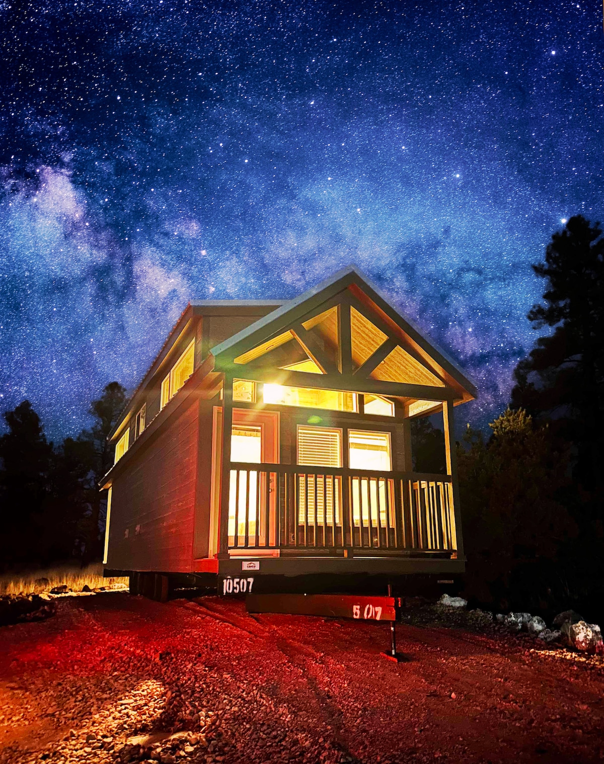 The cozy chalet is illuminated at night, showcasing a welcoming entrance with a porch and a striking architectural design. The backdrop features a starry sky, enhancing the serene ambiance of the natural surroundings.