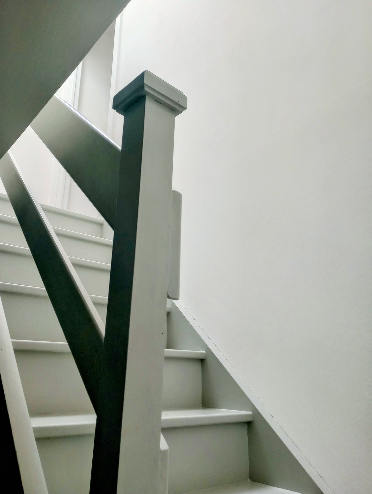A staircase is featured with sleek, light-colored steps leading upward. A minimalist, gray balustrade is seen on one side, contrasting with the plain white walls, creating a clean and bright atmosphere.