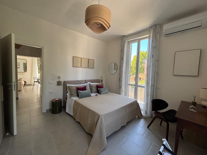 La camera da letto di Suite Vallombrosa ti accoglie con un morbido letto matrimoniale, due comodini di design, un comodo armadio 2 ante, una scrivania d'epoca, la poltroncina, Alexa Spot, aria condizionata, il termosifone ed un simpatico balconcino.