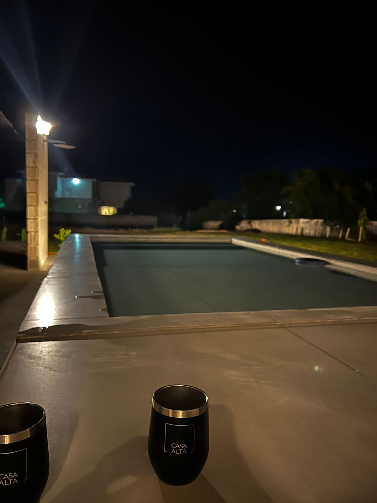 The outdoor area features a well-lit swimming pool surrounded by a spacious lawn. Soft lighting from nearby fixtures highlights the pool's edges, creating a serene atmosphere for evening relaxation.