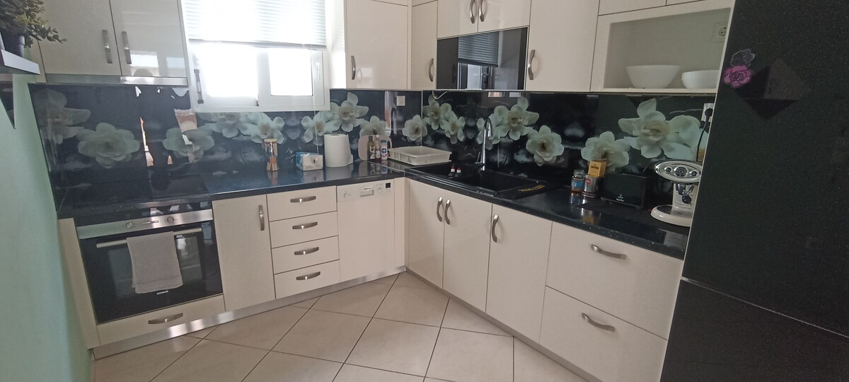 A modern kitchen features stylish cabinetry with a floral backsplash. Stainless steel appliances, including an oven and a refrigerator, are included. Ample counter space is available for food preparation, complemented by a clean and organized layout with neatly arranged utensils.