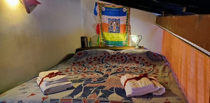 Acogedora cama doble ubicada en la íntima zona del loft, perfecta para momentos de relax con iluminación suave, un rincón de lectura, sábanas suaves y detalles orientales que dan un ambiente único, romántico y envolvente. ¡Un verdadero refugio!