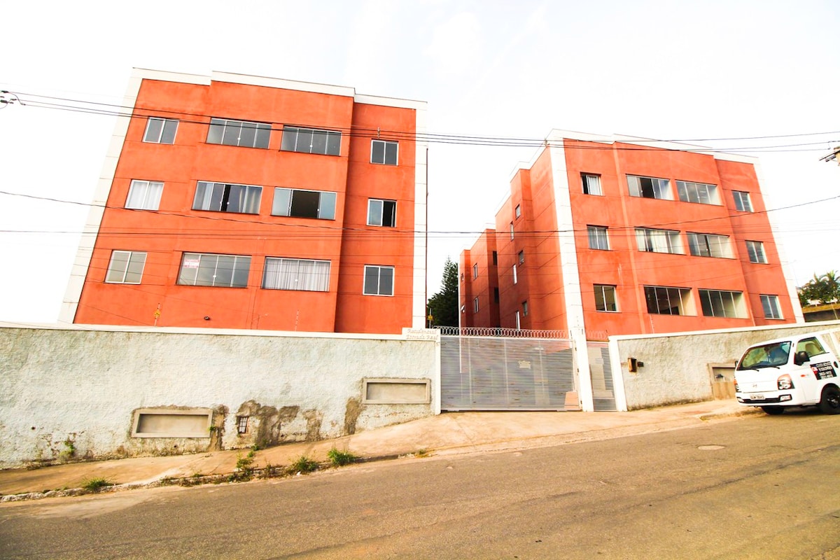 Two modern buildings with a red exterior are seen from the street. Large windows provide ample natural light to the interiors. A secure gate at the entrance adds to the property's privacy, while a light-colored wall outlines the buildings, creating an inviting atmosphere.