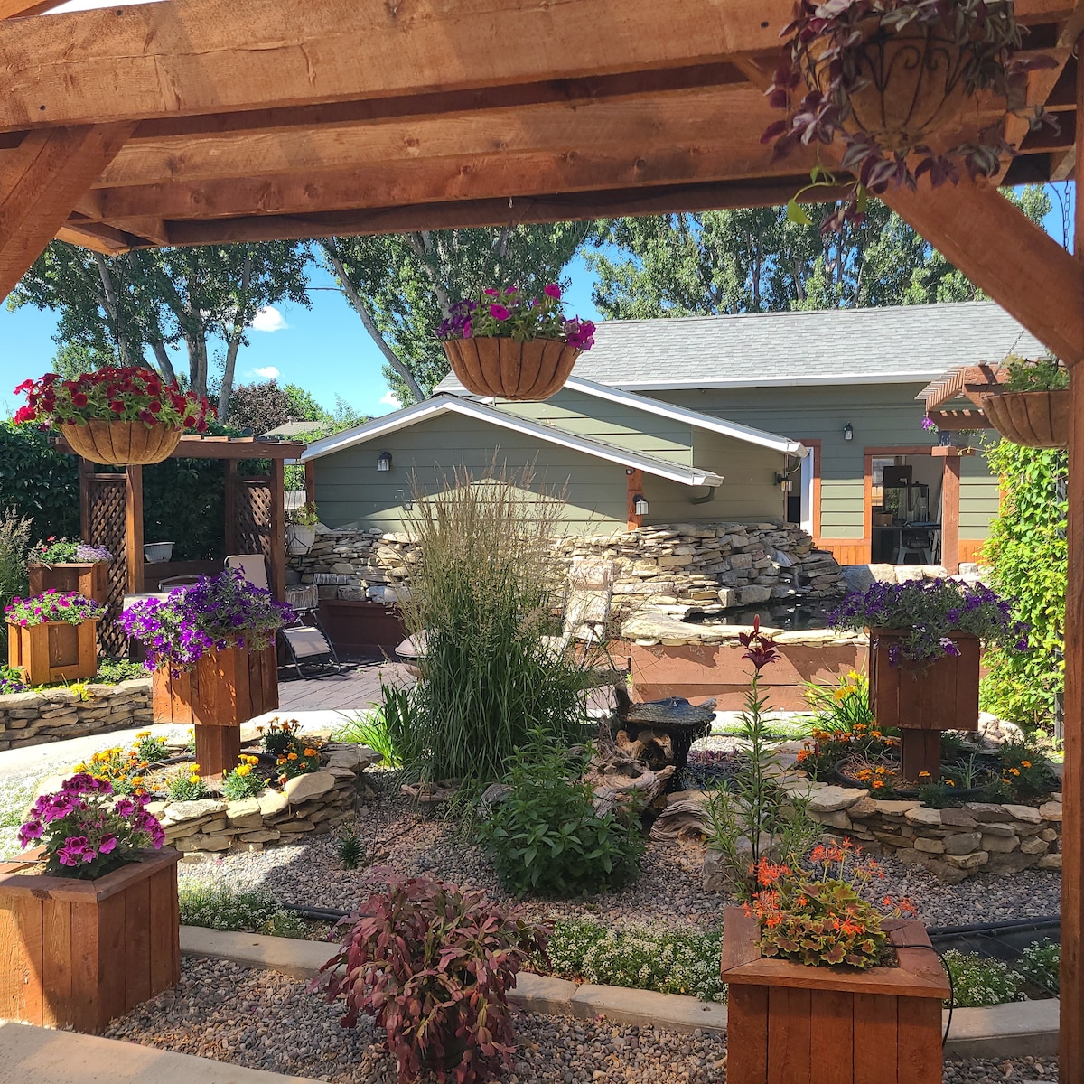 A charming outdoor space features colorful flower arrangements in wooden planters, surrounded by a gravel pathway. A koi pond with a waterfall creates a calming ambiance, while a gazebo structure provides a shaded area to enjoy the serene garden setting.
