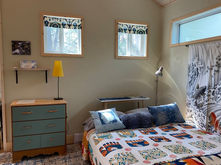 Veľká manželská posteľ s bavlnenými obliečkami, bavlnenou prikrývkou, rúnom  a vlnenými/bavlnenými prikrývkami Pendleton. Dodáva sa flísová prikrývka a vankúše navyše. Lampa na čítanie v rohu.