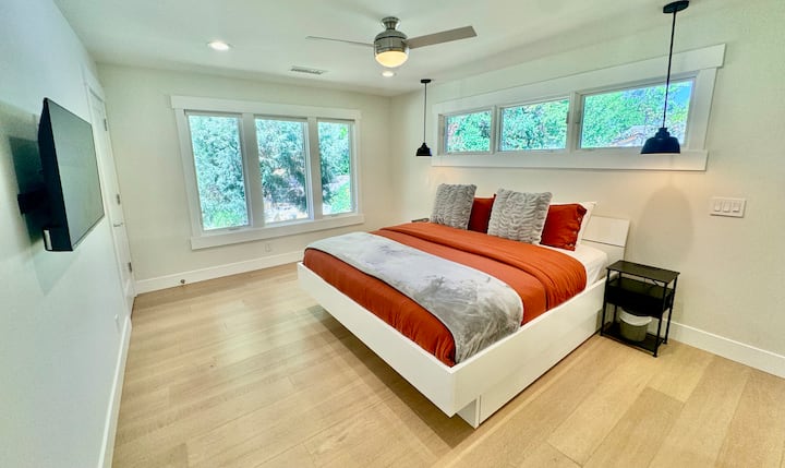 Bright and spacious bedroom retreat. This inviting bedroom features a comfortable bed, large windows with natural light, and a wall-mounted TV—creating a relaxing space to unwind and recharge.