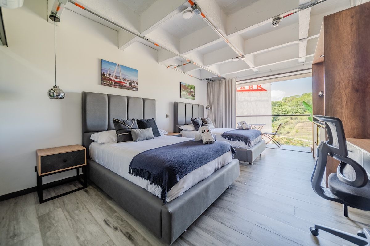 The loft features two spacious beds with soft linens, accented by modern headboards. A window offers views of the greenery outside, while an elegant workspace is positioned beside the balcony. Stylish décor items are placed on the walls, enhancing the overall ambiance.