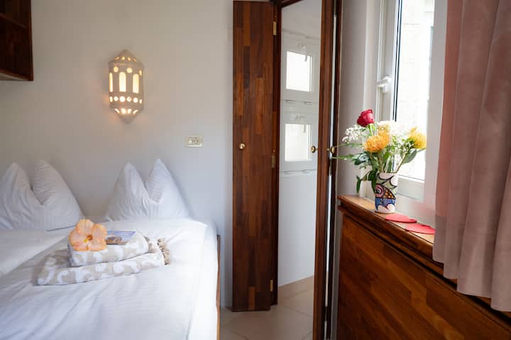 Das Zimmer Mango Nord ist mit wunderschönen Holzmöbel eingerichtet und bietet einen direkten Blick in den Garten. Es verfügt über ein grosses, gemütliches Doppelbett sowie einen Schreibtisch - perfekt zum entspannen und Wohlfühlen.