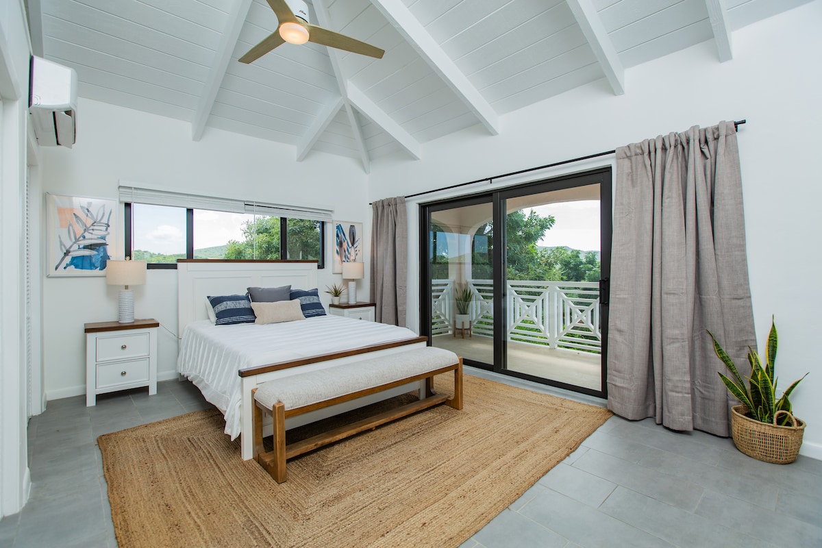 Dormitorio con una cómoda cama tamaño queen, que ofrece vistas relajantes de la vegetación circundante y salida a la terraza de la piscina.  Este dormitorio también tiene baño privado.  