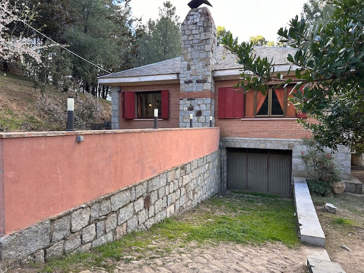Fachada de la casa rural de piedra y ladrillo con garaje: entorno tranquilo en plena sierra.