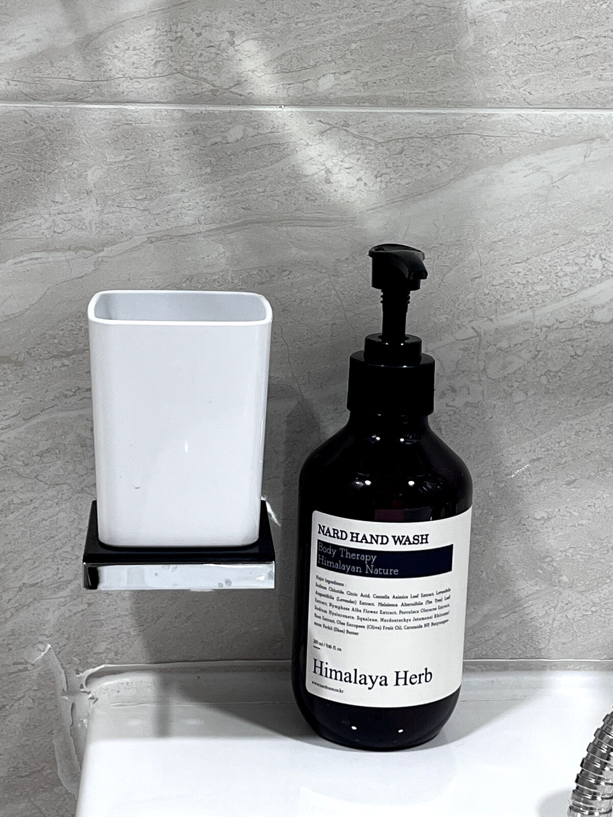 A hand wash station is displayed featuring a pump bottle labeled 'Nard Hand Wash,' accompanied by a white, rectangular container. The countertop is complemented by light-colored tiles, providing a clean and functional atmosphere.