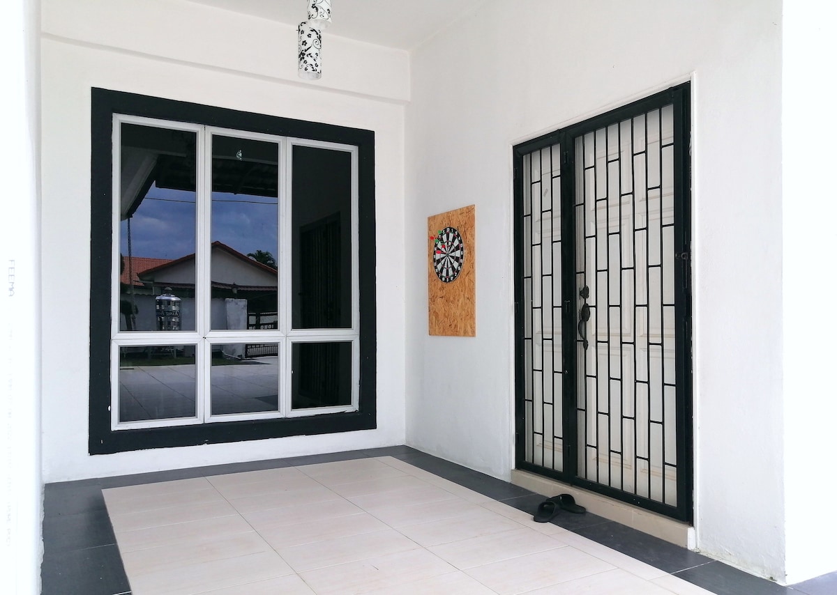 A covered entryway features large glass windows that reflect the surroundings and a stylish black door with a secure metal grille. A dartboard is mounted on the left wall, with a neutral-colored tiled floor providing ample space for socializing.