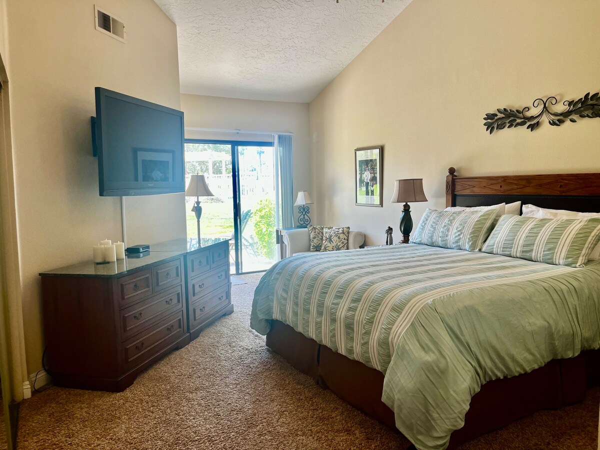 נוף לחדר השינה הראשי. מיטת קינג סייז, שידה, טלוויזיה עם מסך שטוח וכבלים, ארון כפול גדול, כיסא בפינה שקטה עם מנורה לקריאה או לנמנום  ולצד המחוון למרפסת.  