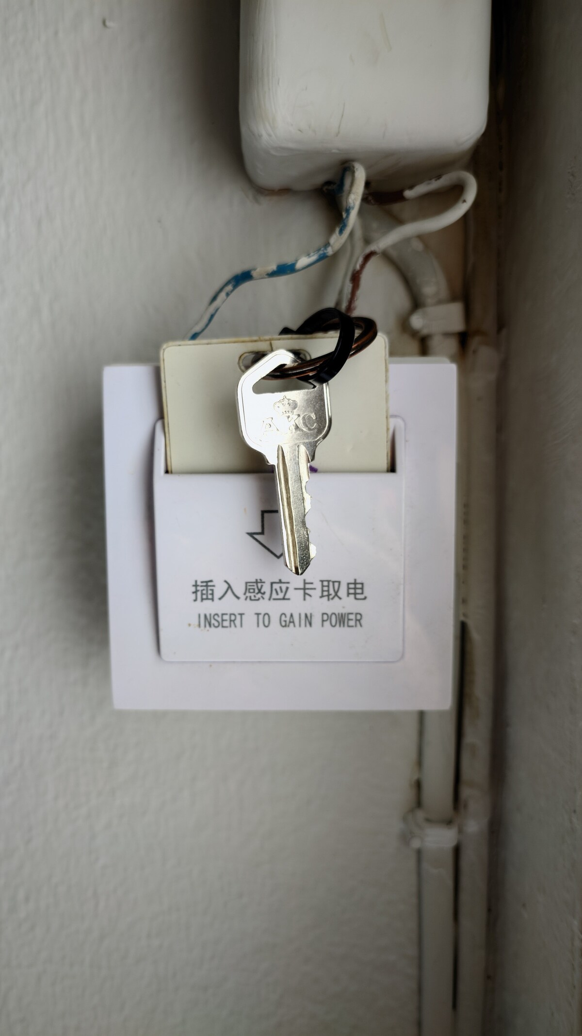 A key is inserted into a power access panel mounted on a wall. The panel features instructions in English and Chinese, indicating how to gain power. The small, rectangular panel is surrounded by visible electrical wiring, suggesting a practical and functional aesthetic.