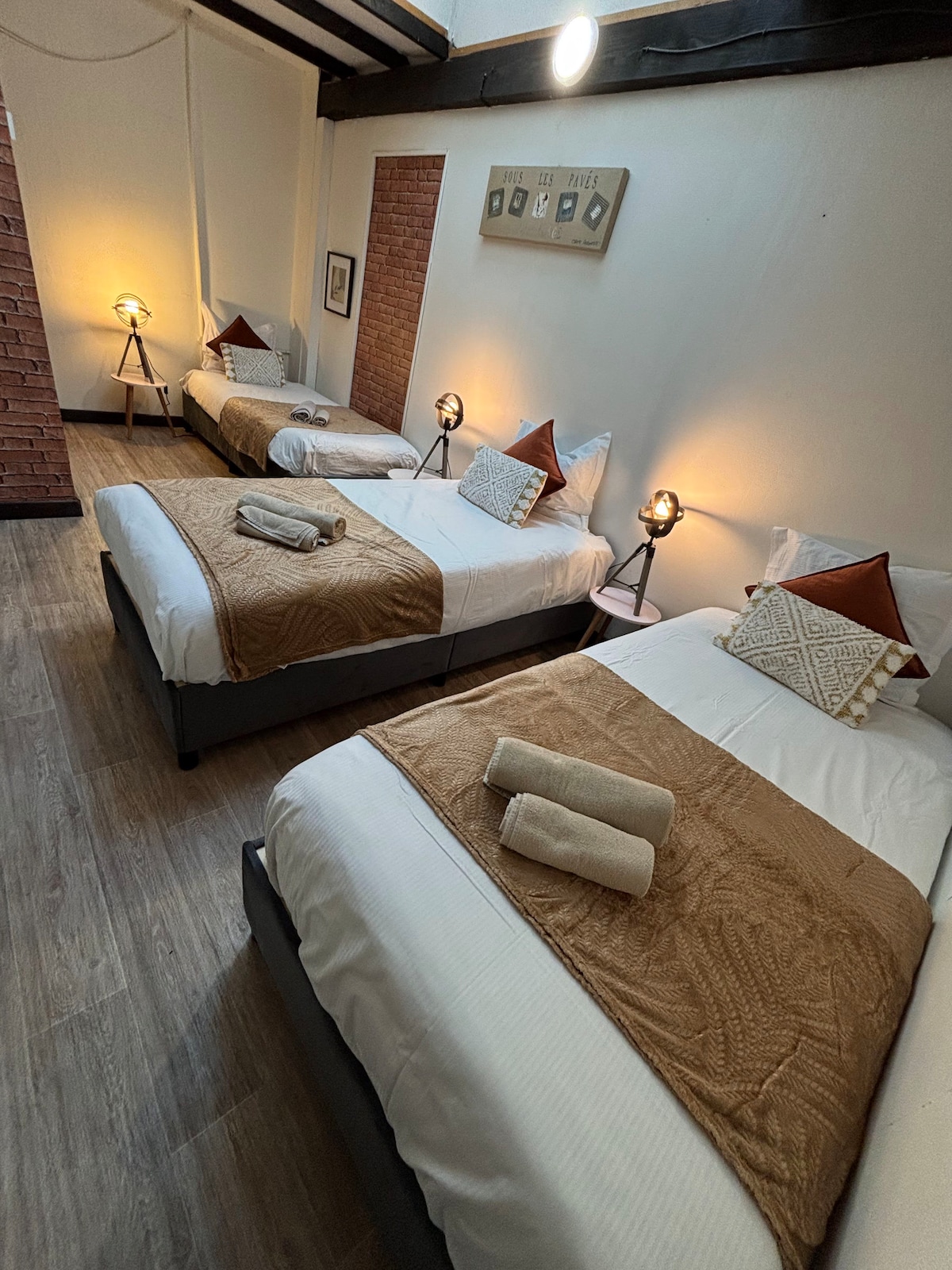 Vista general de la habitación con sus 3 cómodas camas, sábanas limpias y toallas listas para usar, en un ambiente zen.