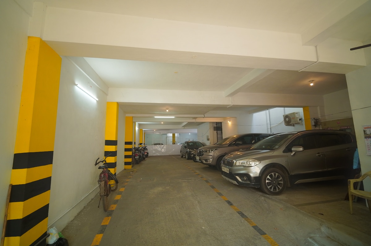 A spacious parking area is illuminated by overhead lights. Vehicles are parked along the sides, with designated lanes marked by yellow lines. The walls are painted white with striking yellow and black stripes, enhancing visibility and safety in the area.