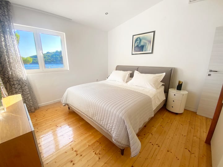 غرفة نوم بإطلالة على البحر بسرير كبير ونوافذ مزدوجة ومصاريع لحجب الضوء.