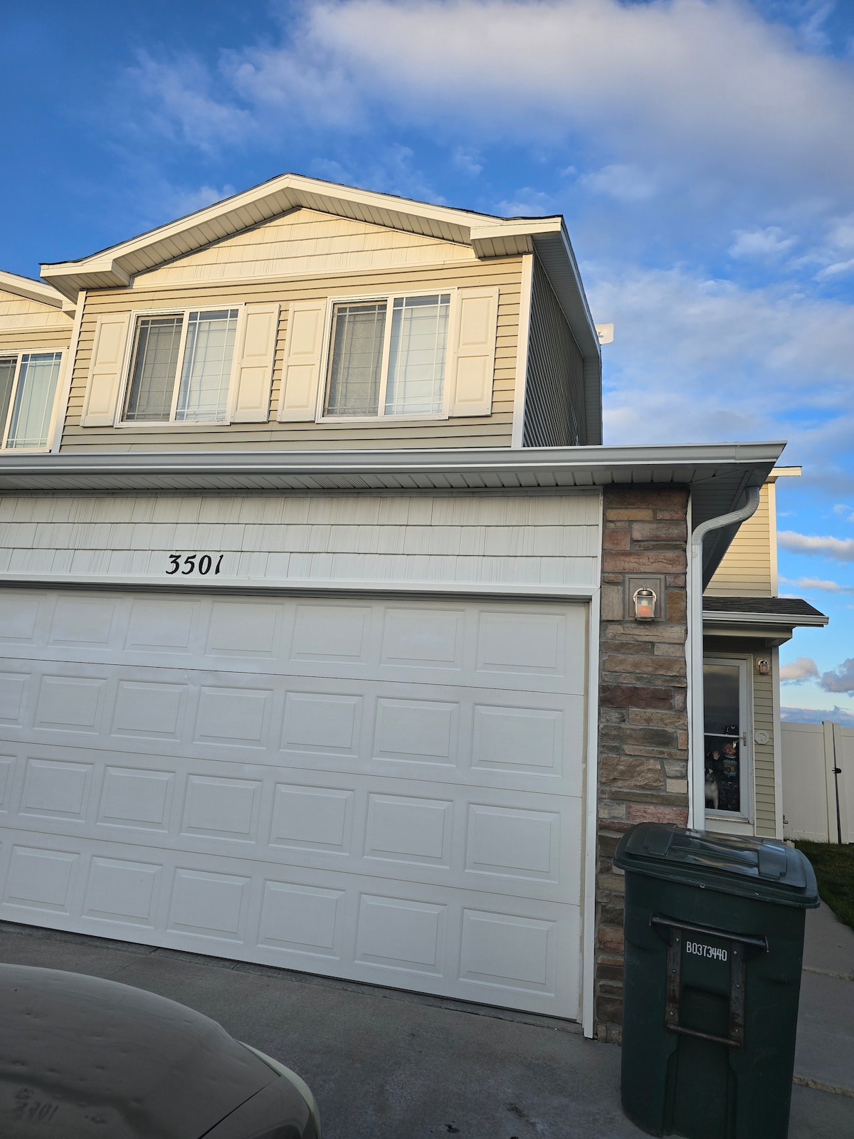 The two-story residence features a light-colored exterior with horizontal siding and stone accents. A double garage door is prominently displayed on the ground level. Large windows allow for ample natural light, contributing to the overall inviting appearance of the home.