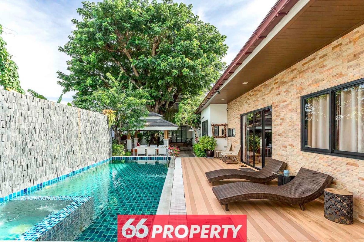 A serene outdoor space features a tranquil swimming pool with a mosaic tile border. Comfortable loungers occupy the wooden deck, while lush greenery and a shaded sala create a relaxing atmosphere, inviting moments of leisure and relaxation.