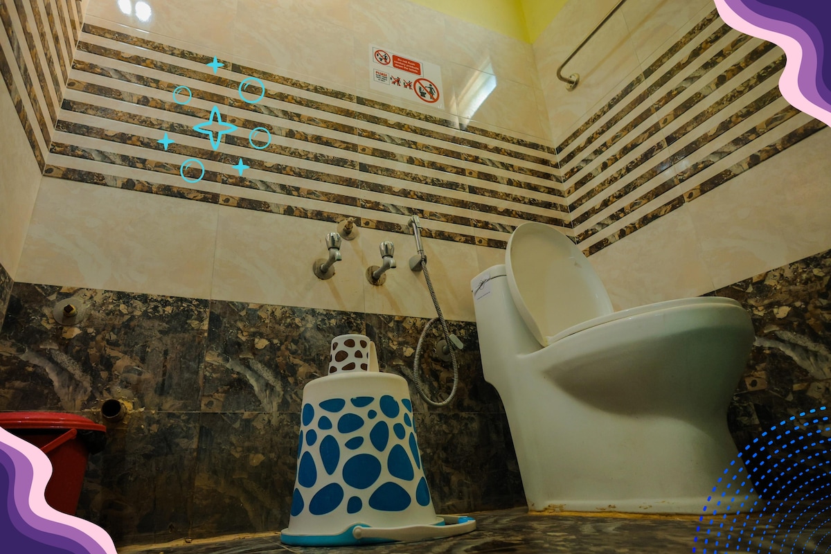 A clean bathroom is presented, featuring a western-style toilet and a small blue-and-white stool nearby. The walls are adorned with a striped tile design, and the floor is covered with dark speckled tiles, providing a practical and functional space.