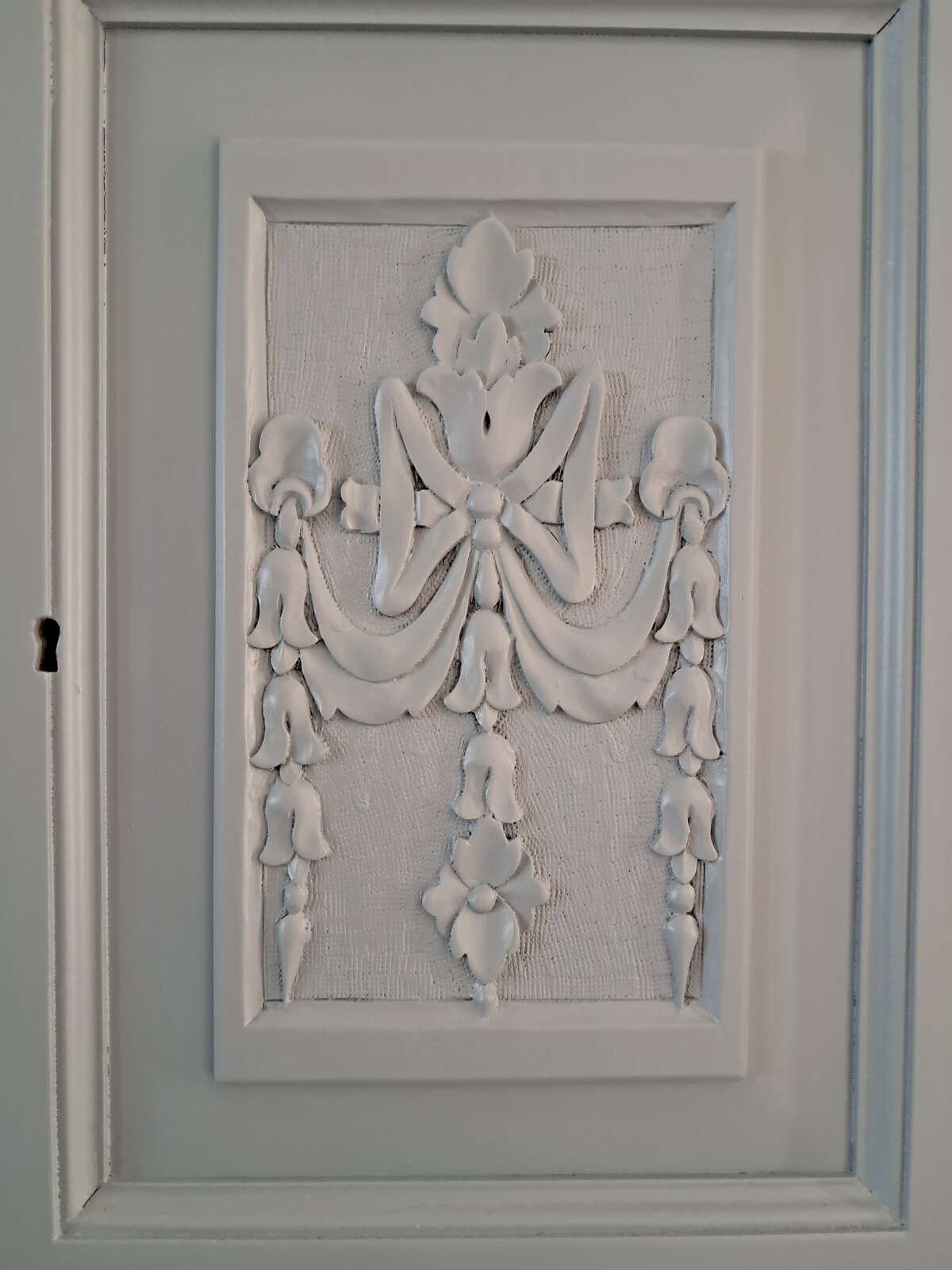 A detailed decorative panel is featured on a light grey cabinet door, showcasing intricate carvings that depict flowing motifs. The texture of the panel contrasts with the smooth surface of the door, adding depth and interest to the design.