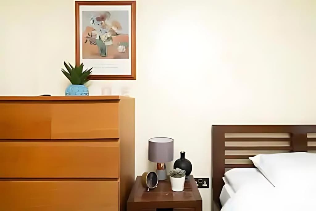 Tavolinë pranë krevatit me abazhur dhe dollapë për ruajtje