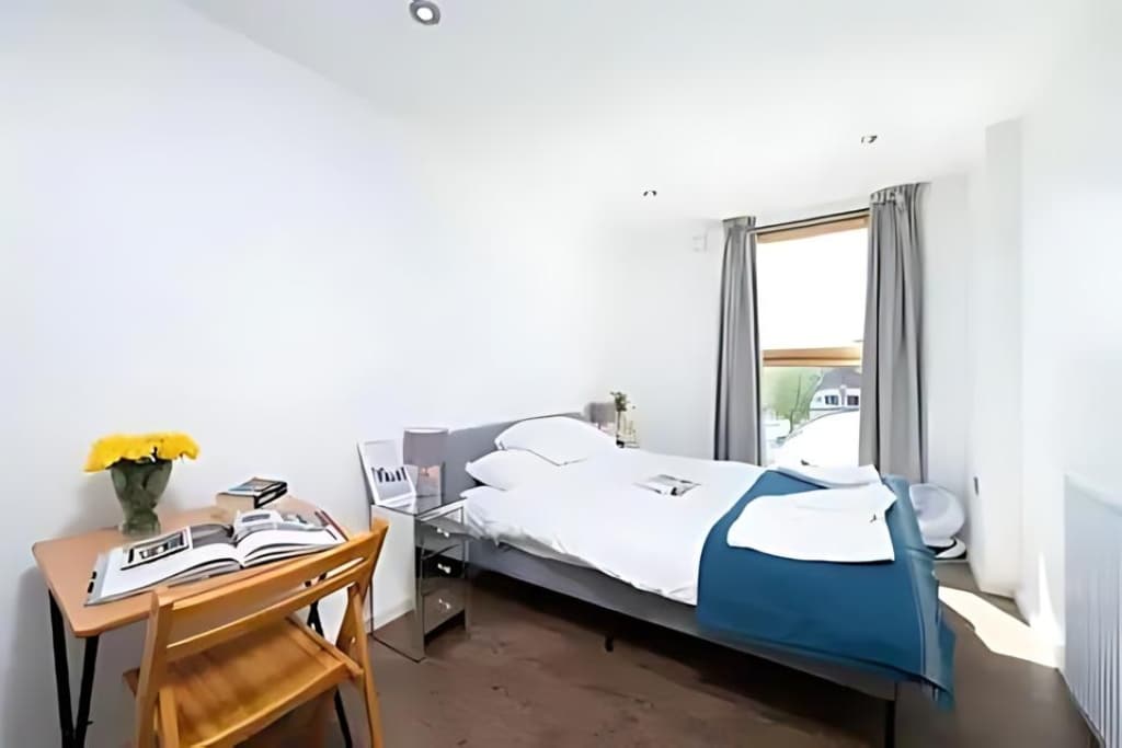 Pamje e gjerë e dhomës së gjumit me krevat dopio, dritare të madhe dhe tavolinë për hapësirën e punës