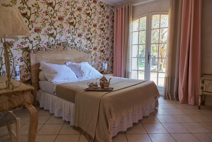 Chumba cha kupendeza kilicho na mapambo ya ukuta wa maua na rangi ya mchanga na maua ya waridi. 
Kitanda cha starehe kilicho na dirisha linaloangalia bustani ya kijani kibichi. 
Mazingira ya joto na mapumziko kwa ajili ya ukaaji wa kupumzika.