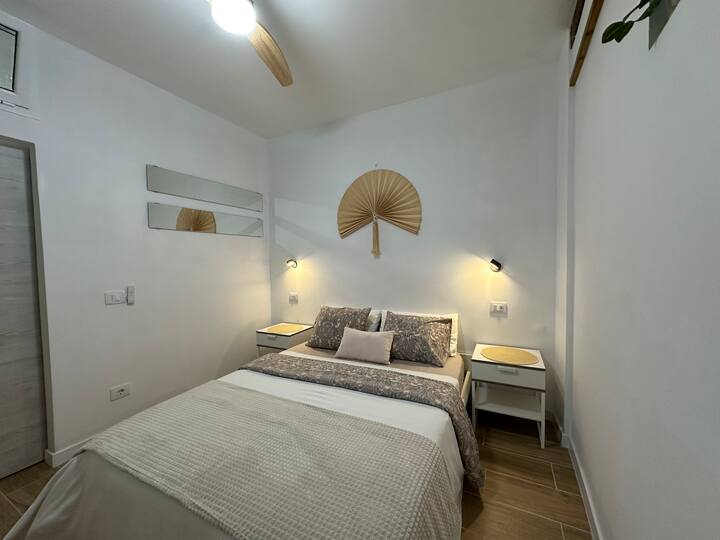 La habitación tiene una cama doble tamaño queen con colchón medianamente firme, mesitas de noche, lámparas de lectura LED, enchufe con conector USB y un control remoto de varias velocidades y ventilador de techo habilitado para WFI.