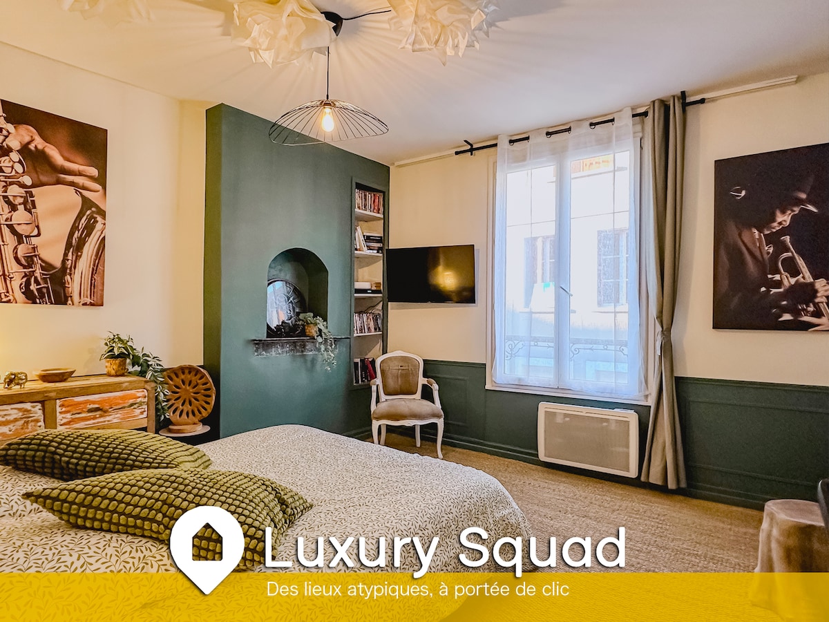 A thoughtfully designed bedroom features a spacious bed adorned with patterned bedding. The walls display framed artwork, while a window allows natural light to brighten the room. A small bookshelf and a decorative shelf complement the cozy atmosphere, enhancing the room's charm.