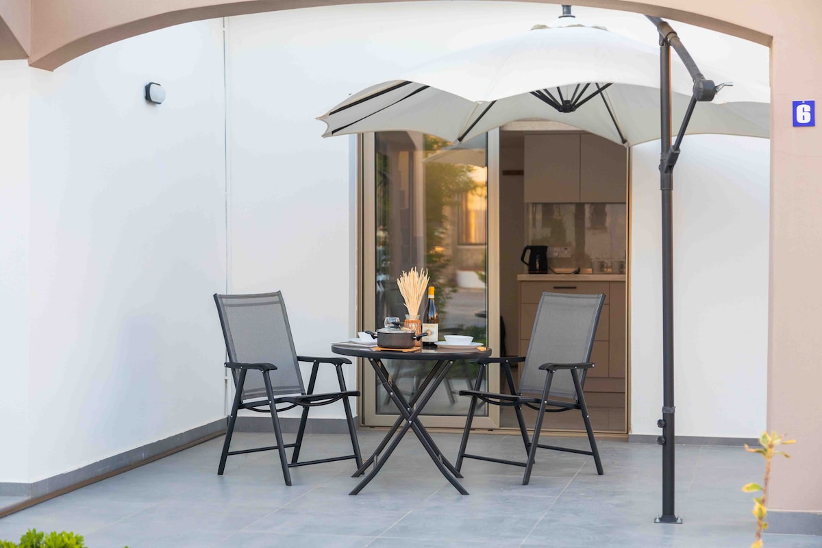 A private outdoor patio features a round table with two chairs, shaded by a large umbrella. This space is designed for relaxed outdoor dining or enjoying drinks, surrounded by a clean, modern aesthetic characteristic of the beachside bungalow.