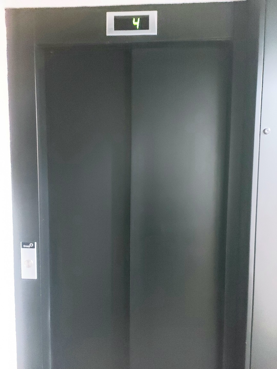 The elevator door is shown in a sleek black finish, with a small panel above displaying the number four. The area appears clean and modern, providing access to upper floors.