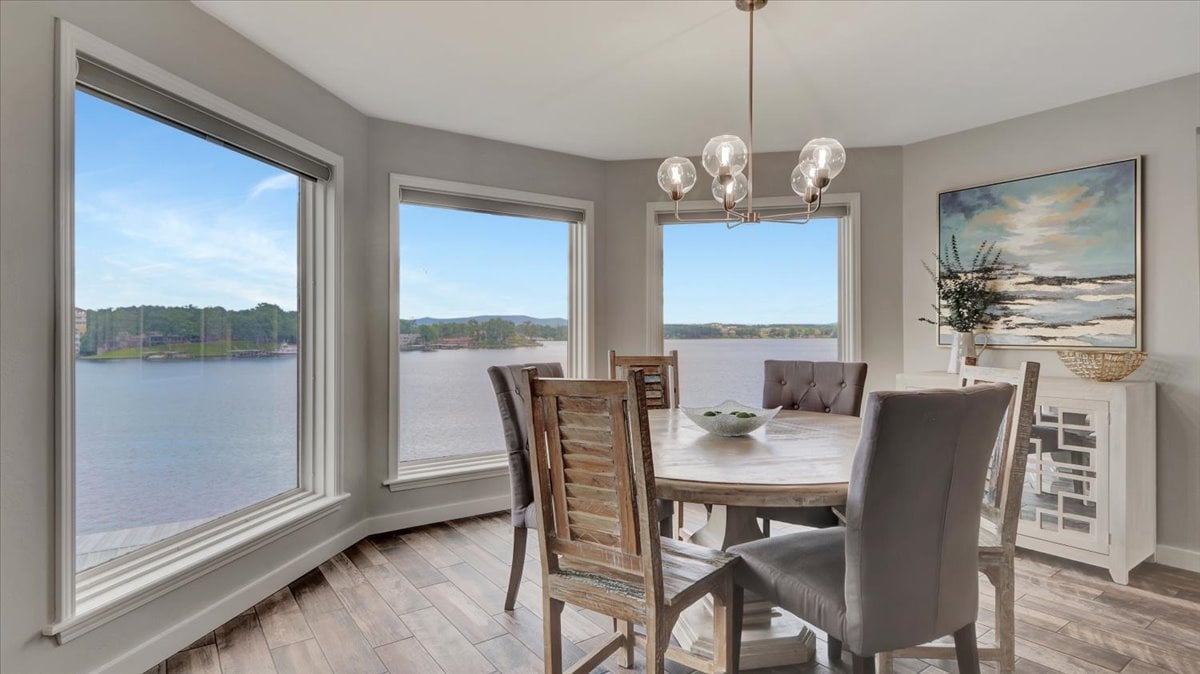 A dining area is highlighted by large, panoramic windows offering views of Lake Hamilton. A round wooden table is surrounded by six chairs, while a sideboard and a piece of artwork adorn the walls, creating a bright and inviting space.