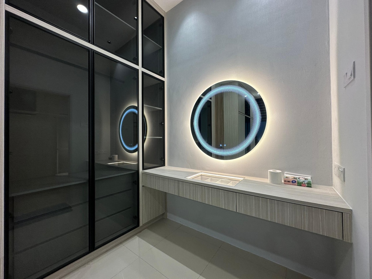 A modern vanity area is illuminated by a circular mirror with a soft glow, reflecting a sleek and minimalist design. The countertop features a tray and a roll of tissue, while the cabinets provide a stylish storage solution. Glossy surfaces enhance the contemporary feel.