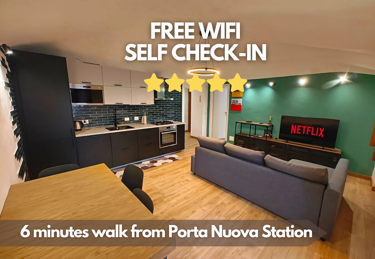 The living area features a modern design with a comfortable sofa bed and a multifunctional table for dining or working. A smart TV is mounted on the wall, providing entertainment options. The space is brightened by natural light, enhancing the cozy atmosphere.