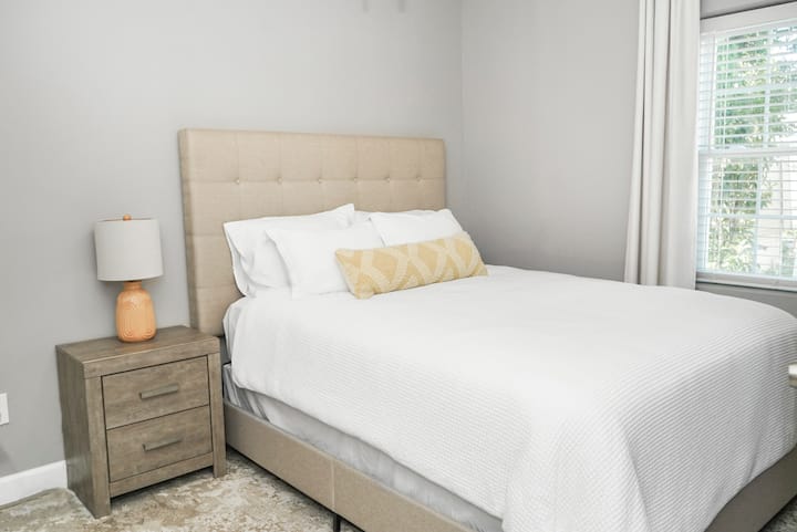 ห้องนอนที่อบอุ่นนี้มีผนังสีเทานุ่มเตียงนอนสบายพร้อมผ้าปูที่นอนสีขาวกรอบและหน้าต่างบานใหญ่ที่ช่วยให้แสงธรรมชาติทำให้ที่พักสว่างขึ้น การออกแบบที่เรียบง่ายและทันสมัยสร้างบรรยากาศที่สงบและผ่อนคลาย