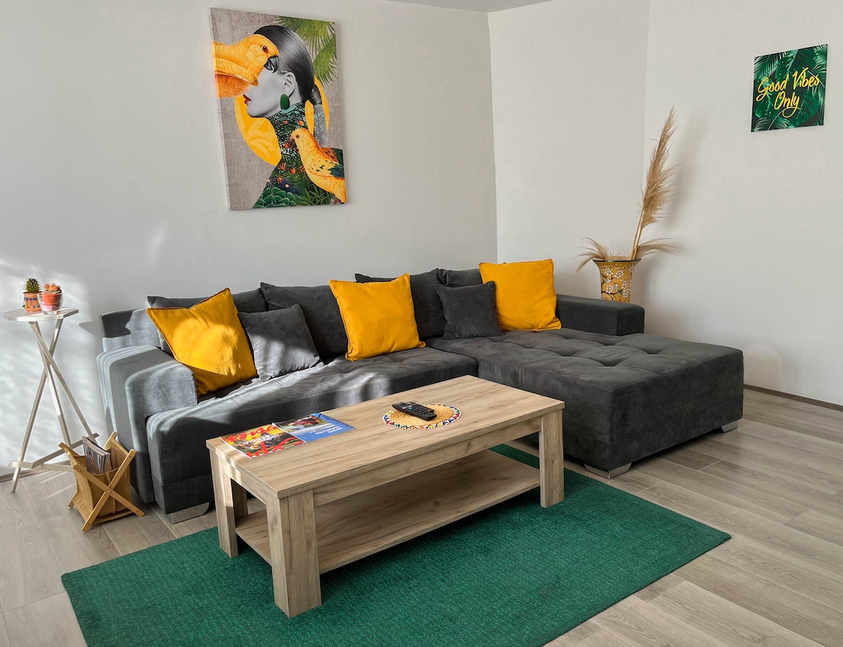 ผ่อนคลายในที่พักสไตล์โมเดิร์นที่มีแสงแดดส่องถึงมีโซฟารูปตัว L ที่สะดวกสบายการตกแต่งที่มีชีวิตชีวาและศิลปะบนผนังที่ไม่เหมือนใคร