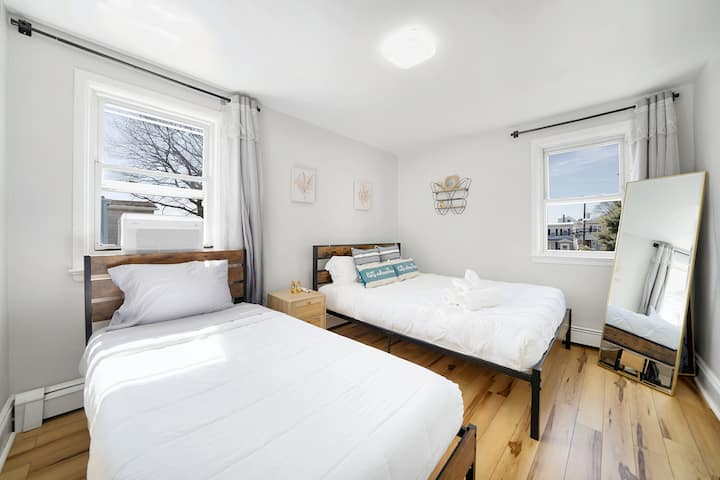 Luchtige slaapkamer met twee eenpersoonsbedden met moderne houten bedden, speelse 'let's adventure'-kussens en zonlicht in overvloed.