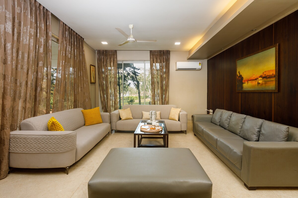 Teplá a príjemná obývačka s plyšovými sedadlami, elegantnou výzdobou a výhľadom do záhrady cez veľké okná – ideálna na rodinné stretnutia, filmové večery alebo spoločný oddych v našej vile Karjat so 4 spálňami.