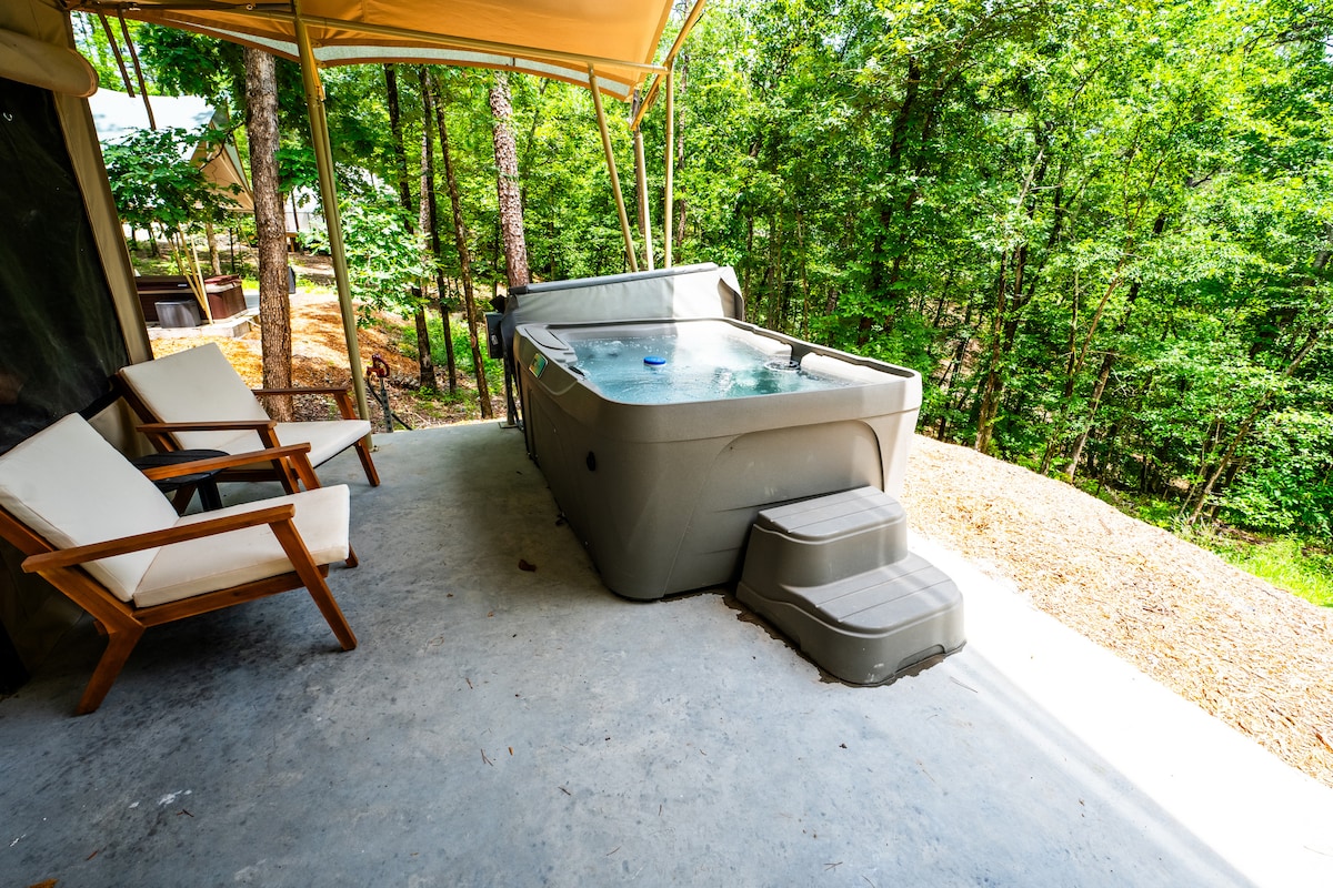 A private deck is featured, showcasing a hot tub with steps leading up to it. Two comfortable lounge chairs are positioned nearby, surrounded by lush greenery that enhances the serene atmosphere.