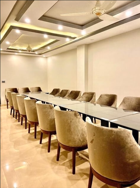 A modern conference room is presented, featuring a long rectangular table surrounded by plush, neutral-colored chairs. A smooth ceiling is adorned with recessed lighting, casting a soft glow over the tiled floor.