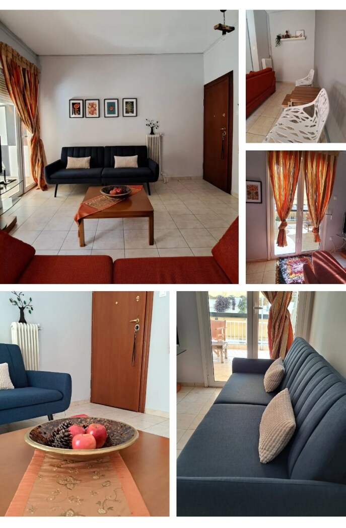 A cozy living area features a mix of upholstered seating in shades of blue and red. Natural light filters through large windows adorned with patterned curtains. A wooden coffee table sits at the center, complemented by decorative items. Vibrant wall art adds a touch of character.